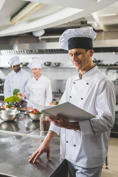 Receita de leitura de chef sorridente na cozinha do restaurante — Fotografia de Stock