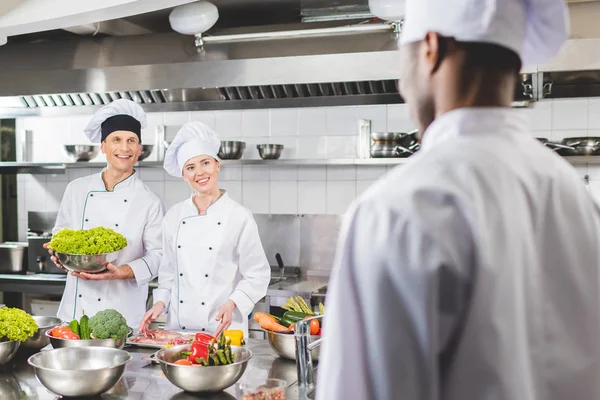 Des chefs multiculturels souriants se regardant à la cuisine du restaurant — Photo de stock