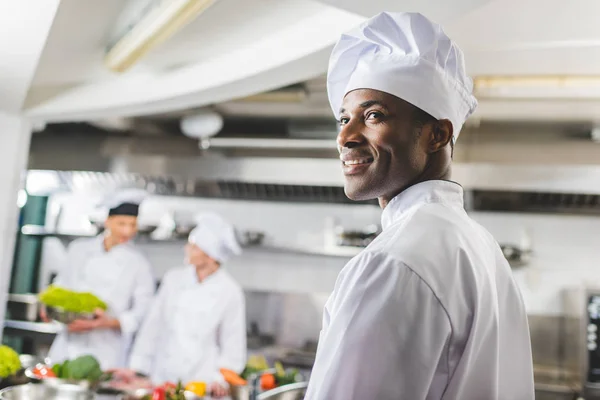 Sonriente afroamericano chef mirando hacia otro lado en la cocina del restaurante - foto de stock