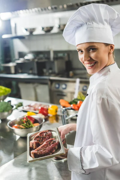 Attractive chef holding tray with raw meat at restaurant kitchen — Stock Photo