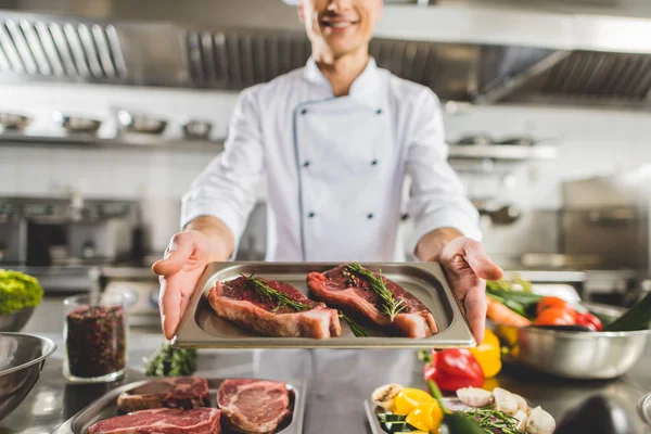 Image recadrée du chef tenant plateau avec des steaks crus à la cuisine du restaurant — Stock Photo