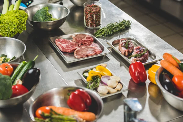 Carne cruda con verduras en la mesa en la cocina del restaurante - foto de stock