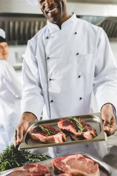 Afrikanisch-amerikanischer Koch hält Tablett mit rohem Fleisch in der Restaurantküche — Stockfoto