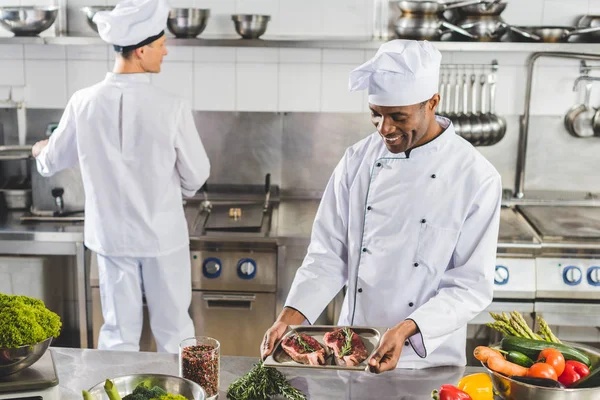 Chefs multiculturais cozinhar carne com legumes na cozinha do restaurante — Fotografia de Stock