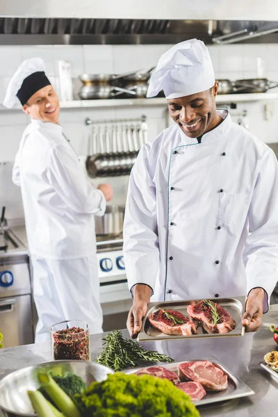 Heureux chefs multiculturels cuisine steaks au restaurant cuisine — Photo de stock
