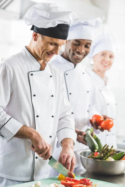 Chefs multiculturales sonrientes cocinando en la cocina del restaurante - foto de stock