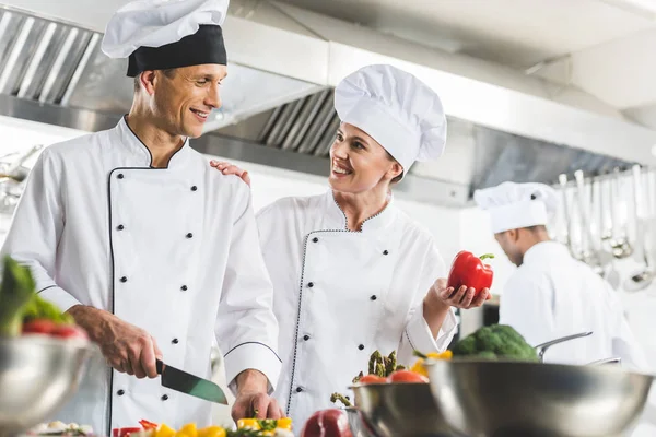 Chef showing bell pepper and palming colleague while he cutting vegetables at restaurant kitchen — Stock Photo