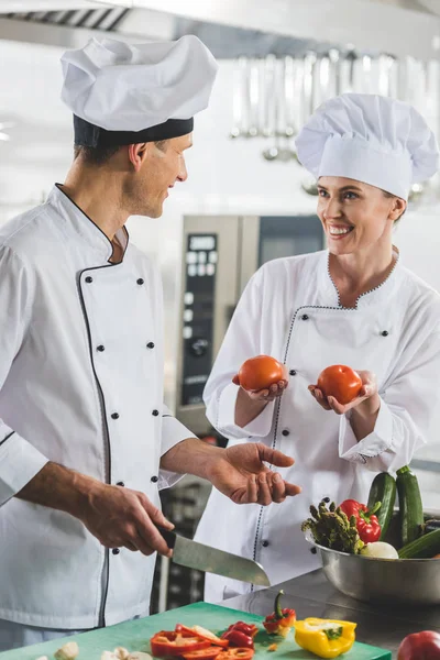 Lächelnder Koch zeigt Kollegen in Restaurantküche reife Tomaten — Stockfoto