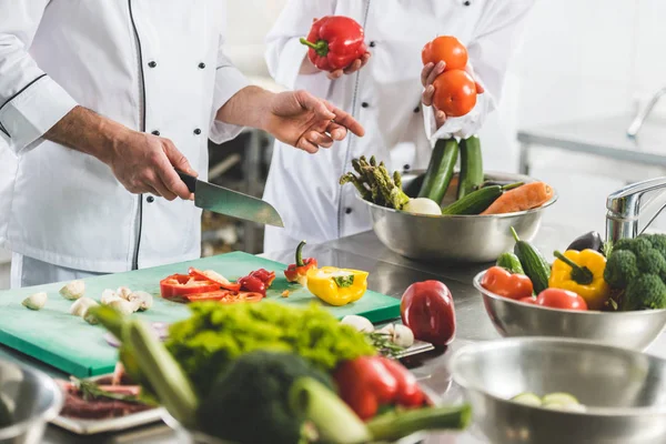Imagen recortada de los chefs preparando verduras en la cocina del restaurante - foto de stock