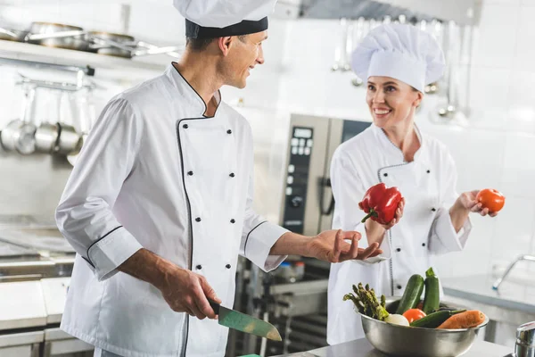 Chef sonriente dando pimiento rojo a colega en la cocina del restaurante - foto de stock