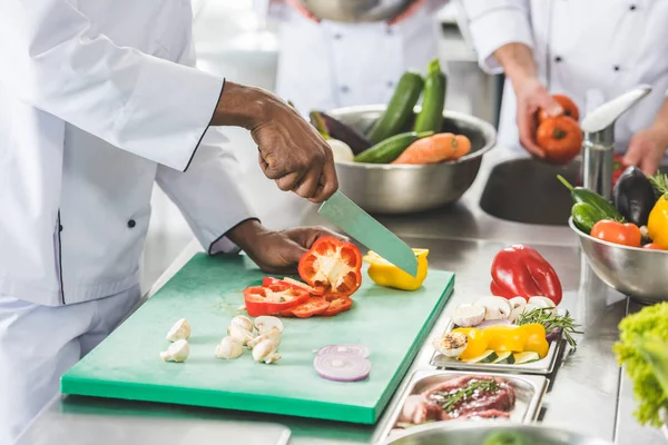 Imagen recortada de chefs multiculturales cortando y lavando verduras en la cocina del restaurante - foto de stock