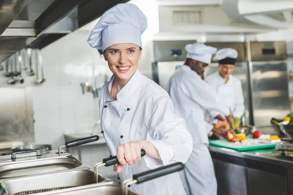 Attractive chef frying food in oil at restaurant kitchen and looking away — Stock Photo