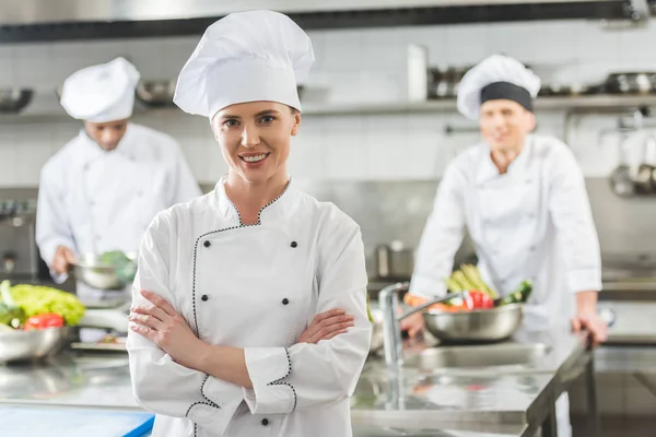 Chef sorridente in piedi con le braccia incrociate e guardando la fotocamera alla cucina del ristorante — Foto stock