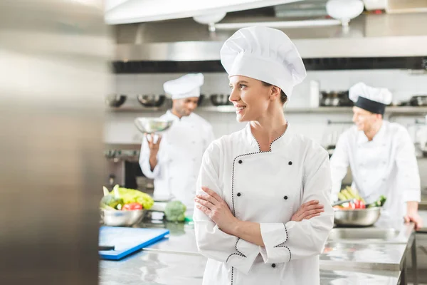 Chef sorridente in piedi con le braccia incrociate e guardando la cucina del ristorante — Foto stock