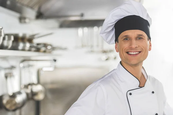 Щасливий красивий шеф-кухар дивиться на камеру на кухні ресторану — стокове фото