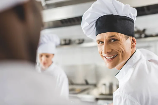 Guapo y sonriente chef mirando a la cámara en la cocina del restaurante - foto de stock