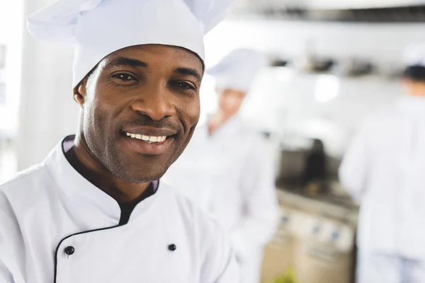 Felice chef africano americano guardando la fotocamera alla cucina del ristorante — Foto stock