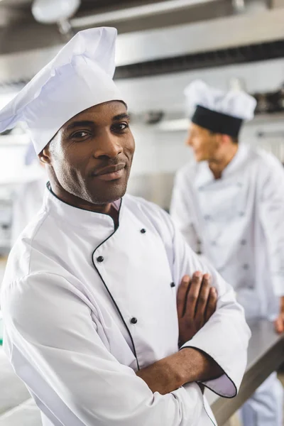 Guapo afroamericano chef mirando la cámara con los brazos cruzados - foto de stock