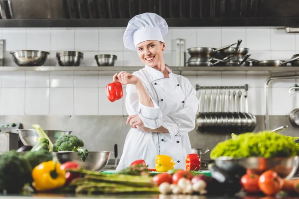 Chef sorrindo segurando pimentão vermelho e olhando para a câmera na cozinha do restaurante — Fotografia de Stock