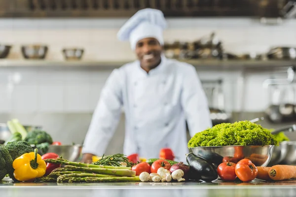 Sonriente chef afroamericano en la cocina del restaurante con verduras en primer plano - foto de stock