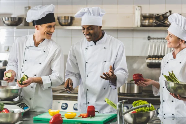 Chefs multiculturales sonrientes hablando en la cocina del restaurante - foto de stock
