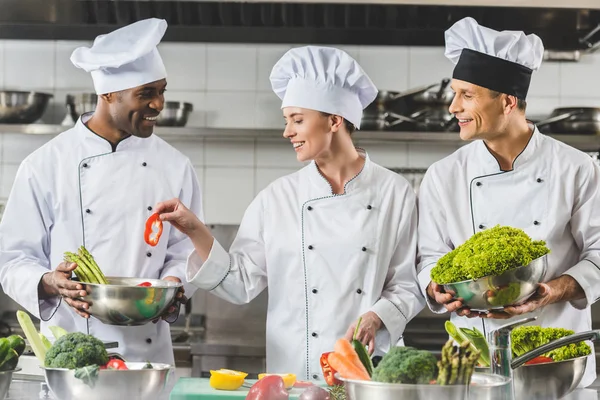Chefs multiculturais felizes cozinhar legumes na cozinha do restaurante — Fotografia de Stock