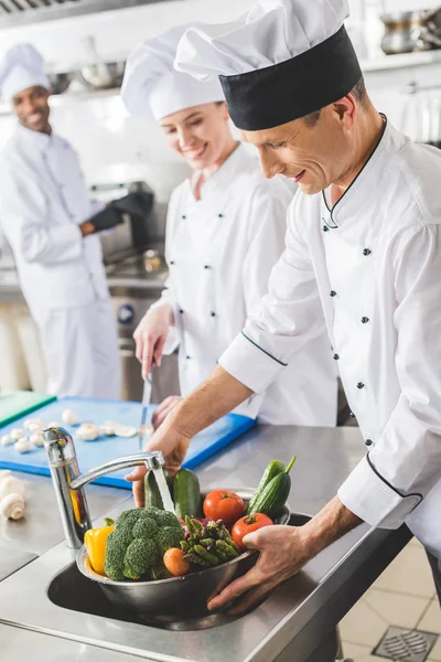 Усміхнений шеф-кухар миє овочі на кухні ресторану — стокове фото