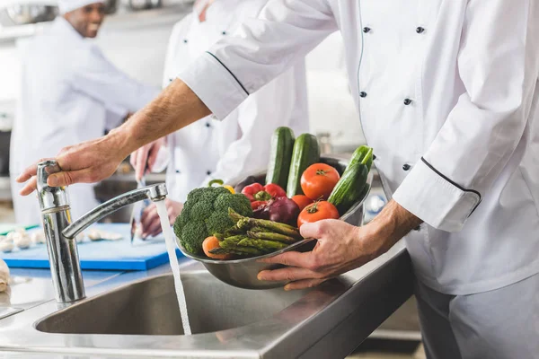 Imagen recortada del chef lavando verduras en la cocina del restaurante - foto de stock
