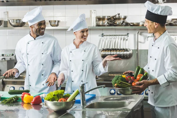 Chefs multiculturales sonrientes hablando en la cocina del restaurante - foto de stock