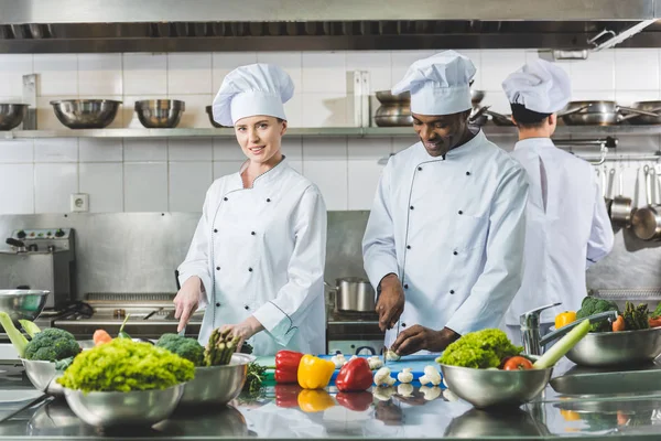 Chefs multiculturels coupant des légumes au restaurant cuisine — Photo de stock