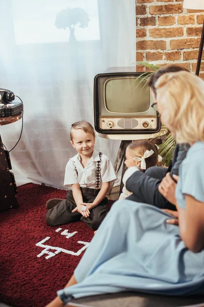 Enfoque selectivo de los padres mirando a los niños adorables jugando en casa, estilo de los años 50 - foto de stock