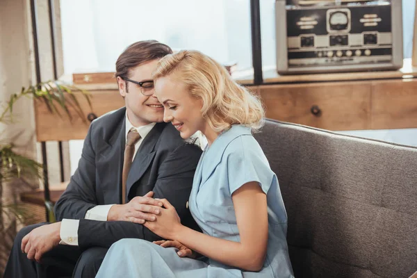 Beautiful happy couple sitting on sofa and holding hands, 1950s style — Stock Photo