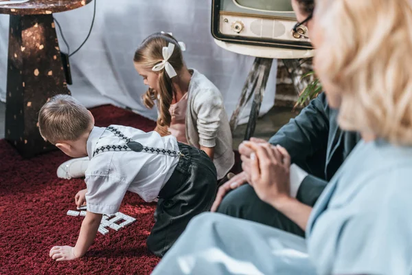 Обрізаний знімок батьків, що сидять на дивані і тримаються за руки, коли діти грають з плиткою доміно, стиль 1950-х років — стокове фото