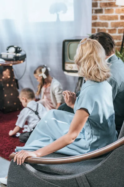 Parents assis sur le canapé et tenant la main pendant que les enfants jouent avec des tuiles domino, style des années 1950 — Photo de stock