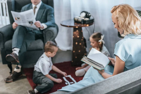 Parents reading book an newspaper while happy kids playing with domino tiles, 1950s style — Stock Photo