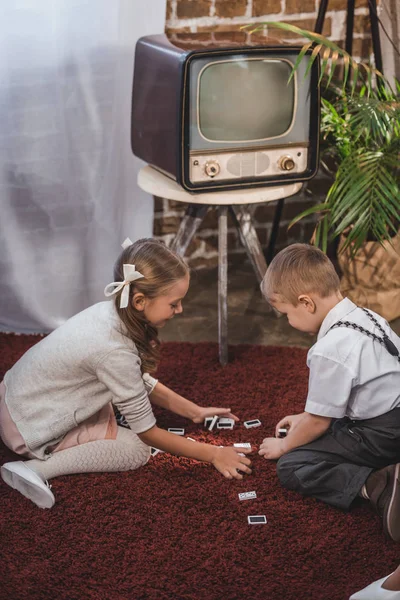 Seitenansicht von niedlichen Kindern, die zu Hause gemeinsam Dominosteine spielen, Stil der 1950er Jahre — Stockfoto