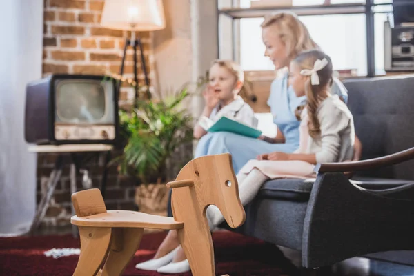 Wooden rocking horse and family reading book behind, 1950s style — Stock Photo