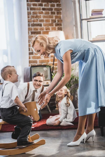 Felice madre, padre e sorella guardando carino bambino seduto su un cavallo a dondolo a casa, stile anni 50 — Foto stock