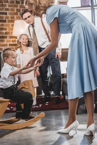 Happy 50s style family looking at cute little boy sitting on rocking horse at home — Stock Photo