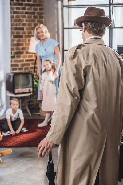 Vista trasera del padre volviendo a casa y mirando a la familia feliz, estilo de los años 50 - foto de stock