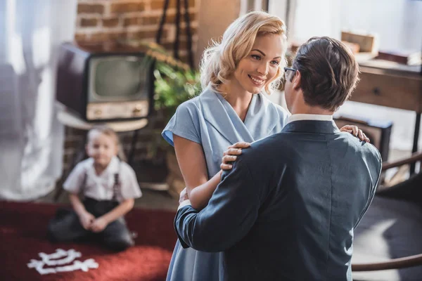 Glückliche Eltern, die einander umarmen und anschauen, während ihr Sohn hinterherspielt, Stil der 1950er Jahre — Stockfoto