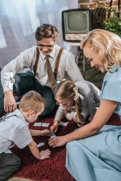 Glückliche Familie mit zwei Kindern, die zu Hause gemeinsam Dominosteine im Stil der 1950er Jahre spielen — Stockfoto