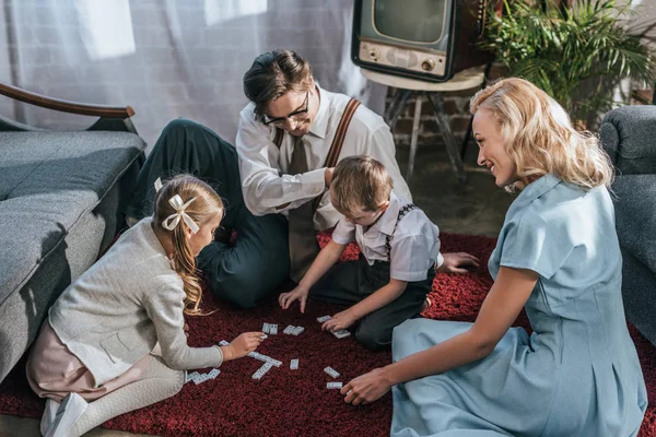 Glückliche Familie mit zwei Kindern, die zu Hause gemeinsam Dominosteine spielen, 50er Jahre — Stockfoto