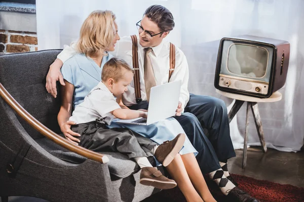 Glückliche Familie im Stil der 50er Jahre mit einem Kind, das zu Hause gemeinsam Laptop benutzt — Stockfoto