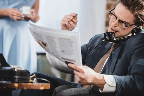Man in suit reading newspaper and talking by vintage telephone — Stock Photo