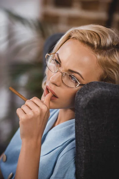 Hermosa mujer rubia en gafas con cigarrillo y mirando hacia otro lado, estilo años cincuenta - foto de stock