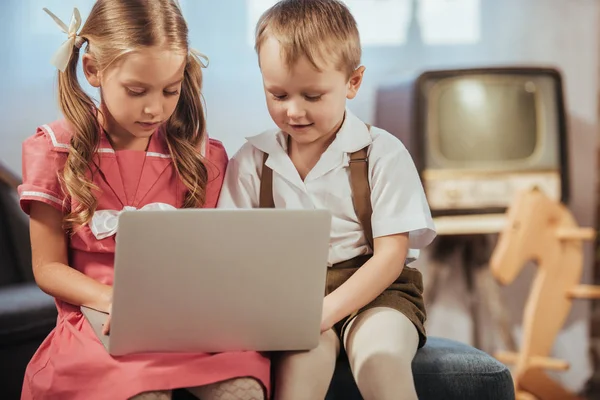 Cute little children in 1950s style clothes using laptop together at home — Stock Photo