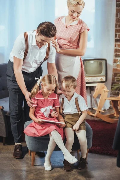 Happy parents looking at cute little kids using digital tablet, 1950s style — Stock Photo