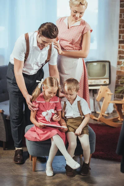 Padres felices mirando a los niños pequeños lindos usando tableta digital, estilo de los años 50 — Stock Photo