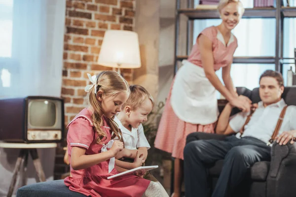 Lächelnde Eltern, die süße kleine Kinder mit einem digitalen Tablet im Vintage-Stil betrachten — Stockfoto